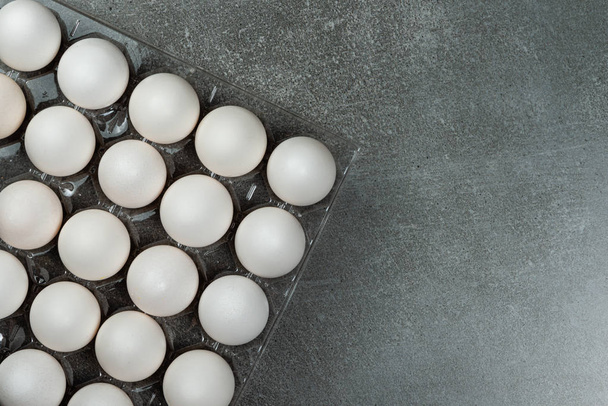 Sok fehér csirke tojást élelmiszer a tálcában. Szürke háttérterület a szöveghez. - Fotó, kép