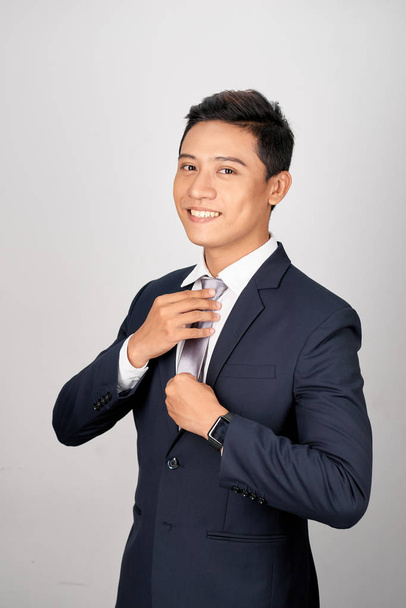 Aziatische zakenman aanpassen grijze stropdas, geïsoleerd op witte achtergrond - Foto, afbeelding
