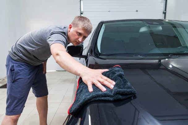 Un trabajador masculino lava un coche negro, limpiando el agua con un paño suave
 - Foto, imagen