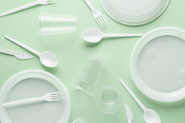 Various white plastic disposable tableware on green background. - Zdjęcie, obraz