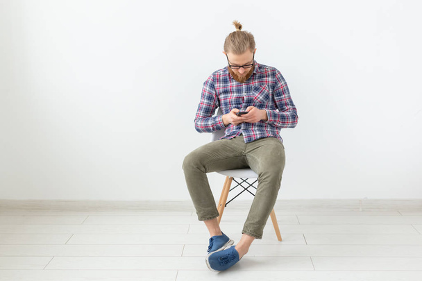 Homem bonito barbudo em camisa xadrez olhando para o celular no fundo branco
 - Foto, Imagem