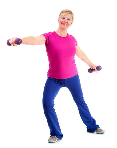 Пенсионерский женский спорт. Полнометражный портрет пожилой женщины занимается спортом. Женщина держит фиолетовые гантели и весело улыбается во время спортивных упражнений. изолированные на белом фоне
 - Фото, изображение
