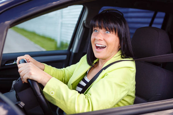 Scared and surprised woman with big eyes holds the steering wheel with both hands shouts driving the car - outdoors - Foto, imagen