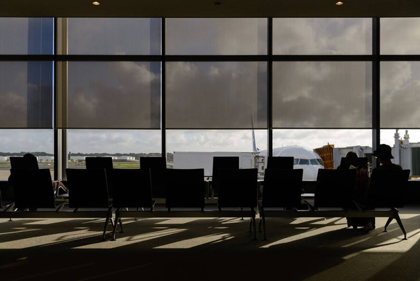 Σιλουέτες συνοδηγού που κάθονται στο σαλόνι αναχώρησης του αεροδρομίου - Φωτογραφία, εικόνα