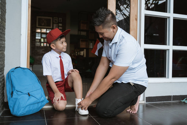 isä auttaa poikaansa valmistautumaan kouluun aamulla
 - Valokuva, kuva