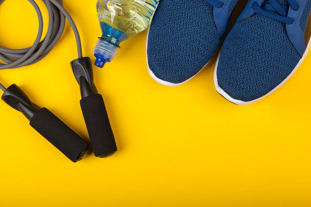 Baskets bleues, corde à sauter et bouteille d'eau sur fond jaune. Concept de mode de vie sain, entraînement quotidien et force de volonté - Photo, image