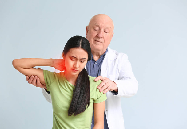 Seniorphysiotherapeutin arbeitet mit jungen Asiatinnen vor hellem Hintergrund - Foto, Bild