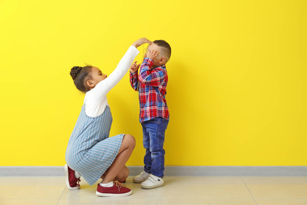 Linda niña afroamericana midiendo la altura de su hermano cerca de la pared de color
 - Foto, imagen