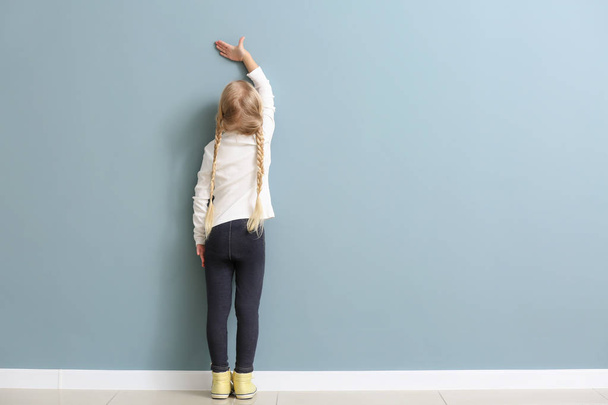 Симпатична маленька дівчинка вимірює висоту біля стіни
 - Фото, зображення