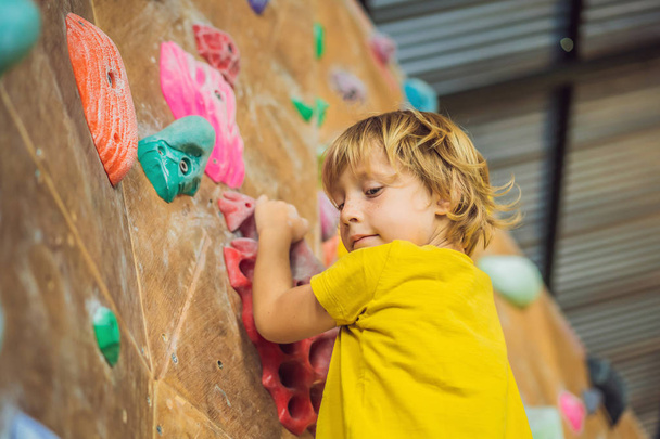 little boy climbing a rock wall in special boots. indoor - 写真・画像