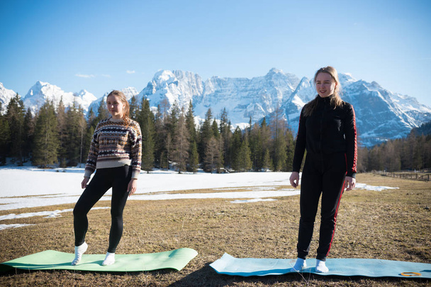 Dolomites - Two young women standing on yoga mats on a background of the forest - Photo, Image