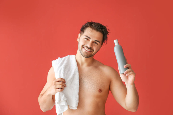 Bello uomo con bottiglia di shampoo e asciugamano su sfondo colore
 - Foto, immagini