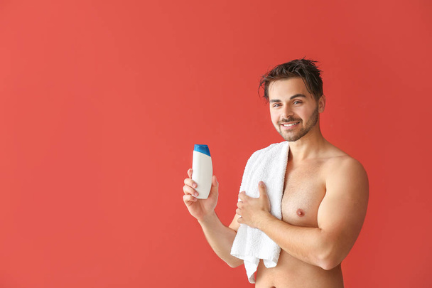 schöner Mann mit einer Flasche Shampoo und Handtuch auf farbigem Hintergrund - Foto, Bild