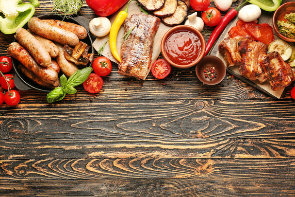 Tasty grilled meat with sausages and vegetables on wooden background - 写真・画像