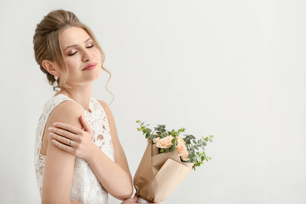 Όμορφη νεαρή νύφη με μπουκέτο λουλουδιών σε λευκό φόντο - Φωτογραφία, εικόνα