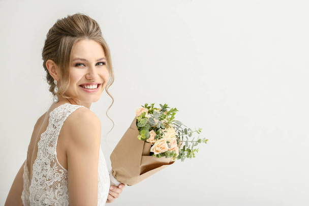 Mooie jonge bruid met boeket bloemen op witte achtergrond - Foto, afbeelding