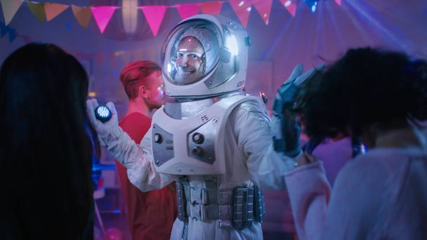 At the College House Costume Party: Fun Guy Wearing Space Suit Dances Off, Doing Robot Dance Modern Moves. With Him Beautiful Girls and Boys Dancing in Neon Lights. - Foto, imagen