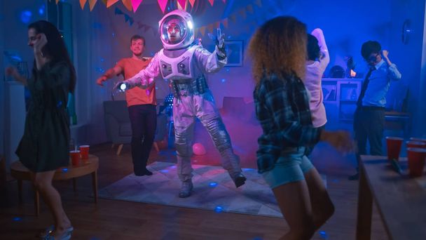 На костюмированной вечеринке в Колледж-хаусе: Веселый парень в космическом костюме танцует, танцует робот современные движения. С Ним танцуют девочки и мальчики в неоновых огнях
. - Фото, изображение
