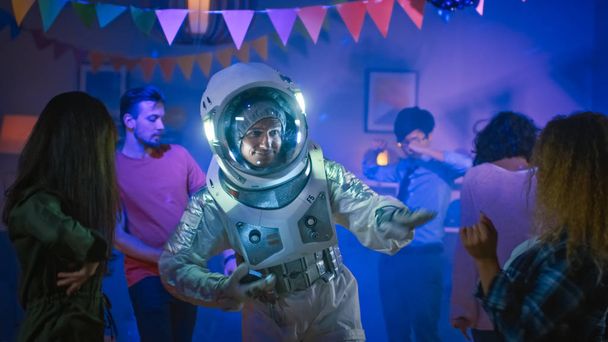 At the College House Costume Party: Fun Guy Wearing Space Suit DAt the College House Costume Party: Fun Guy Wearing Space Suit Dances Off, Doing Robot Dance Modern Moves. With Him Beautiful Girls and Boys Dancing in Neon Lights. - Foto, Bild
