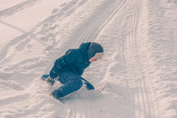 A boy in ski clothing indulges in a snow hill, winter snow frosty weather - Zdjęcie, obraz