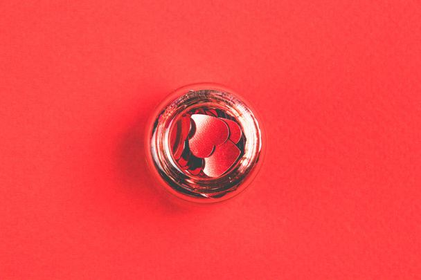 Red confetti in the form of heart in decorative bottle on a red background. Top view. Valenrine`s Day concept. - Foto, Bild