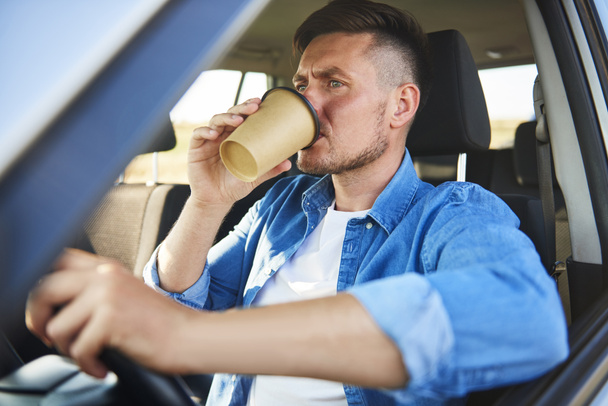 Στρεσαρισμένος άνθρωπος οδηγώντας ένα αυτοκίνητο και πίνοντας καφέ σε μια βιασύνη  - Φωτογραφία, εικόνα