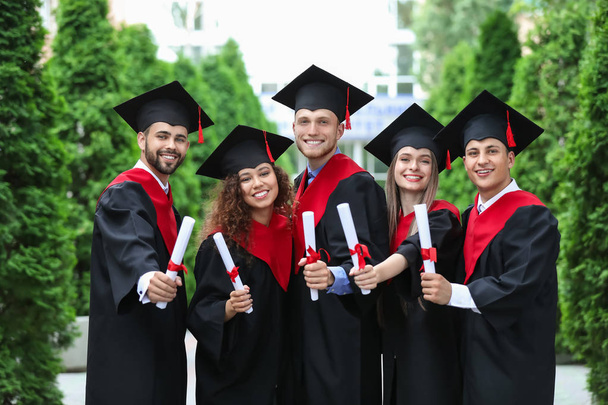 Счастливые студенты в холостяцких одеждах и с дипломами на открытом воздухе
 - Фото, изображение