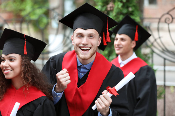 Happy students in bachelor robes outdoors - Valokuva, kuva