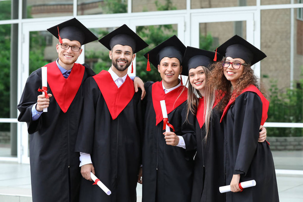 Gelukkige studenten in Bachelor gewaden en met diploma's buitenshuis - Foto, afbeelding