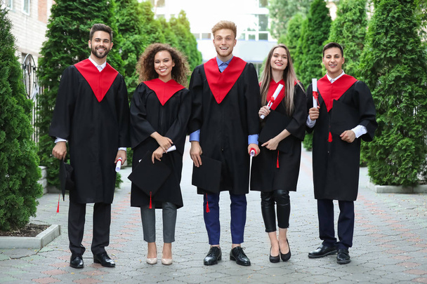 Happy students in bachelor robes outdoors - Photo, Image