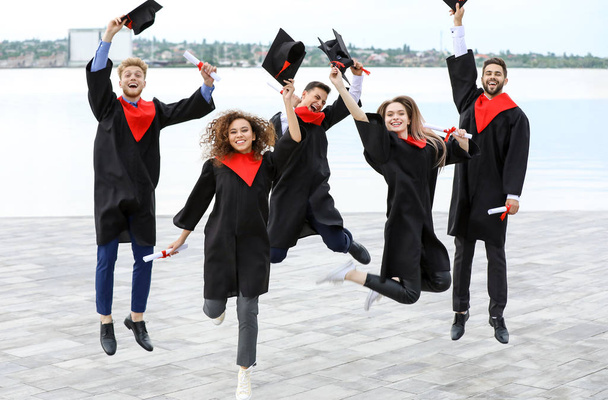 Happy students in bachelor robes outdoors on graduation day - Zdjęcie, obraz