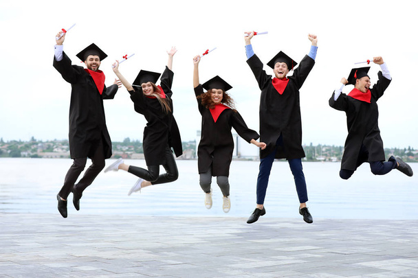 Estudantes felizes em roupões de solteiro e com diplomas ao ar livre
 - Foto, Imagem