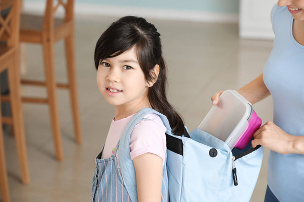 Mãe colocando lancheira na mochila de sua filhinha antes da escola
 - Foto, Imagem