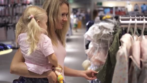 Een vrouw met een kind het kopen van kleren in een kinder winkel. Moeder en dochter in het winkelcentrum. - Video