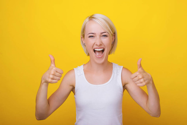 Portret van opgewonden blonde vrouw tonen duimen omhoog over geel b - Foto, afbeelding