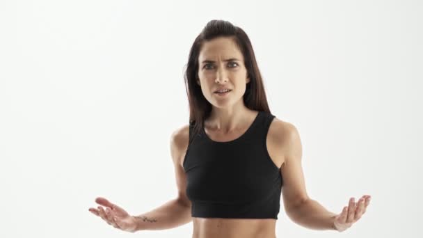 Angry attractive sporty brunette woman in black sportswear arguing with someone and gesturing with hands over white background isolated - Felvétel, videó
