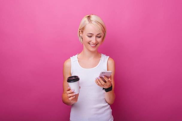 Cheerful woman, using mobile phone and a cup with coffee, standi - Foto, imagen