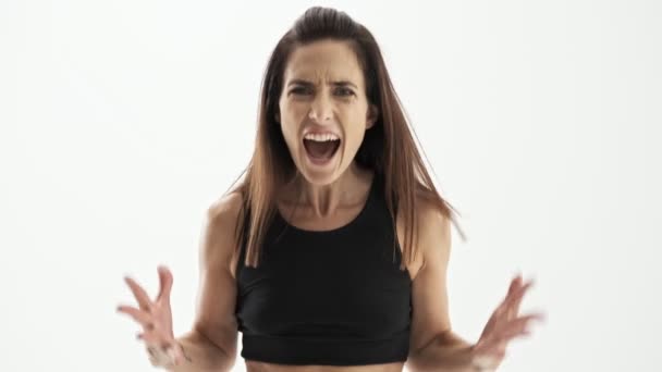 Angry attractive sporty brunette woman in black sportswear screaming very loudly and gesturing with hands over white background isolated - Metraje, vídeo