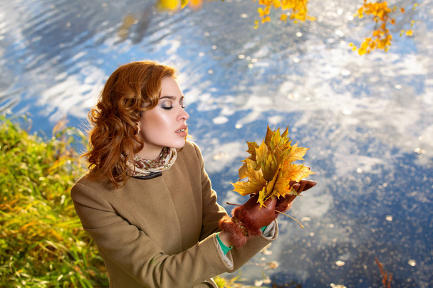 Young woman in the park and holds yellow autumn maple leaves. - Photo, Image