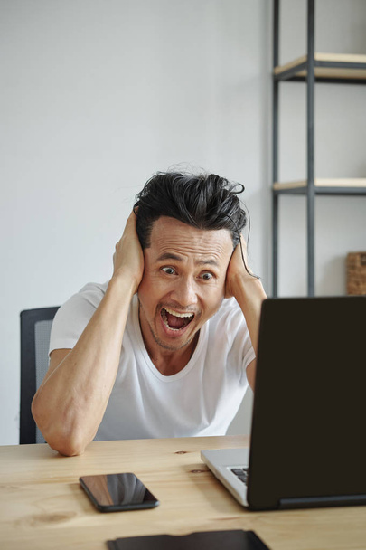 Urlando scioccato uomo vietnamita tenendo la testa durante la lettura di e-mail sullo schermo del computer portatile
 - Foto, immagini