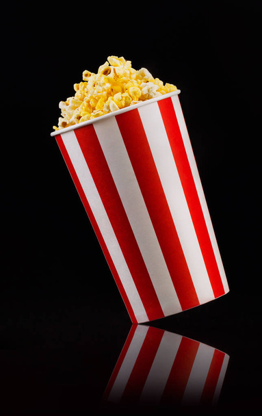 Paper striped bucket with popcorn isolated on black background - Fotó, kép