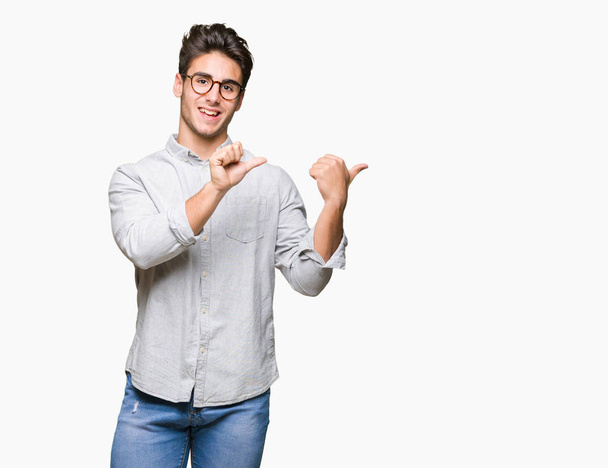 Όμορφος νεαρός φορώντας γυαλιά πάνω από απομονωμένες φόντο δείχνοντας πίσω πίσω από το χέρι με μπράβο, χαμογελώντας αυτοπεποίθηση - Φωτογραφία, εικόνα