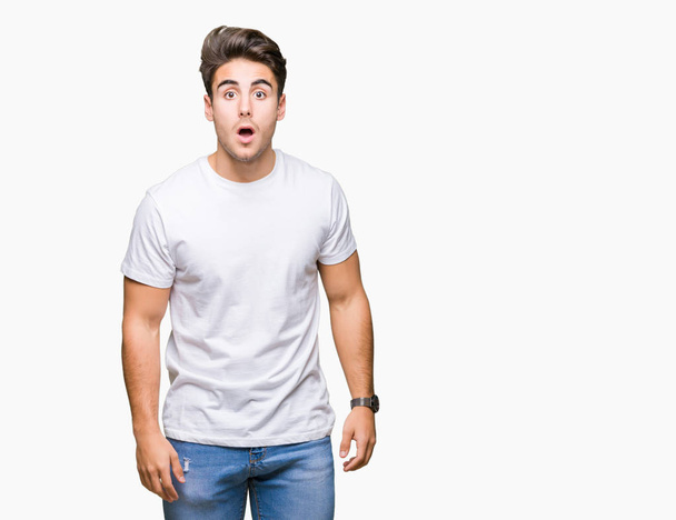 Mladý pohledný muž na sobě bílé tričko izolované pozadí strach a šokován s výrazem překvapení, strach a vzrušený obličej. - Fotografie, Obrázek