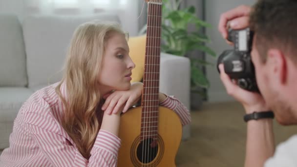 ein junger Mann fotografiert ein Mädchen mit einer Gitarre zu Hause - Filmmaterial, Video
