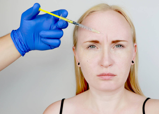Botox injection in the forehead, remove the vertical wrinkle. Young woman on reception at the beautician, the procedure of rejuvenation - Photo, Image