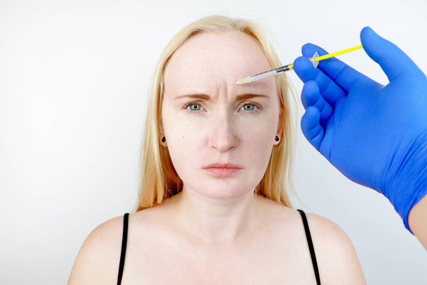 Botox-Injektion in die Stirn, entfernen Sie die senkrechte Falte. junge Frau am Empfang bei der Kosmetikerin, die Prozedur der Verjüngung - Foto, Bild