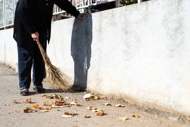 Nő takarítás elesett őszi levelek az utcán - Fotó, kép
