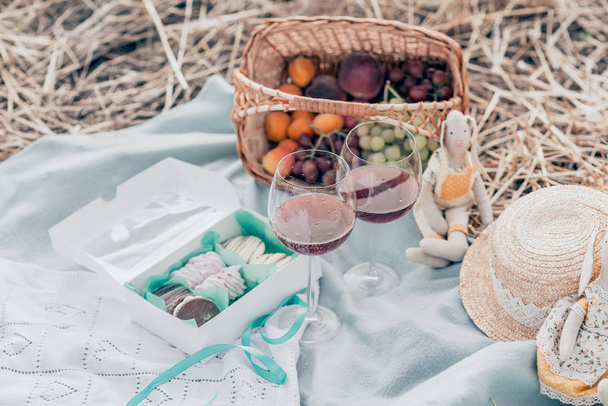 Dwa kieliszki czerwonego wina, owoców i słodyczy na pikniku o zachodzie słońca. - Zdjęcie, obraz
