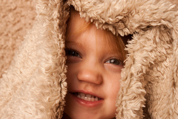 Niño sonriente escondido en una manta de piel
 - Foto, imagen