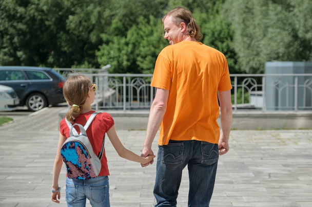 Dad walks with his daughter holding hands. Outdoor, sunny summer day, back view - 写真・画像